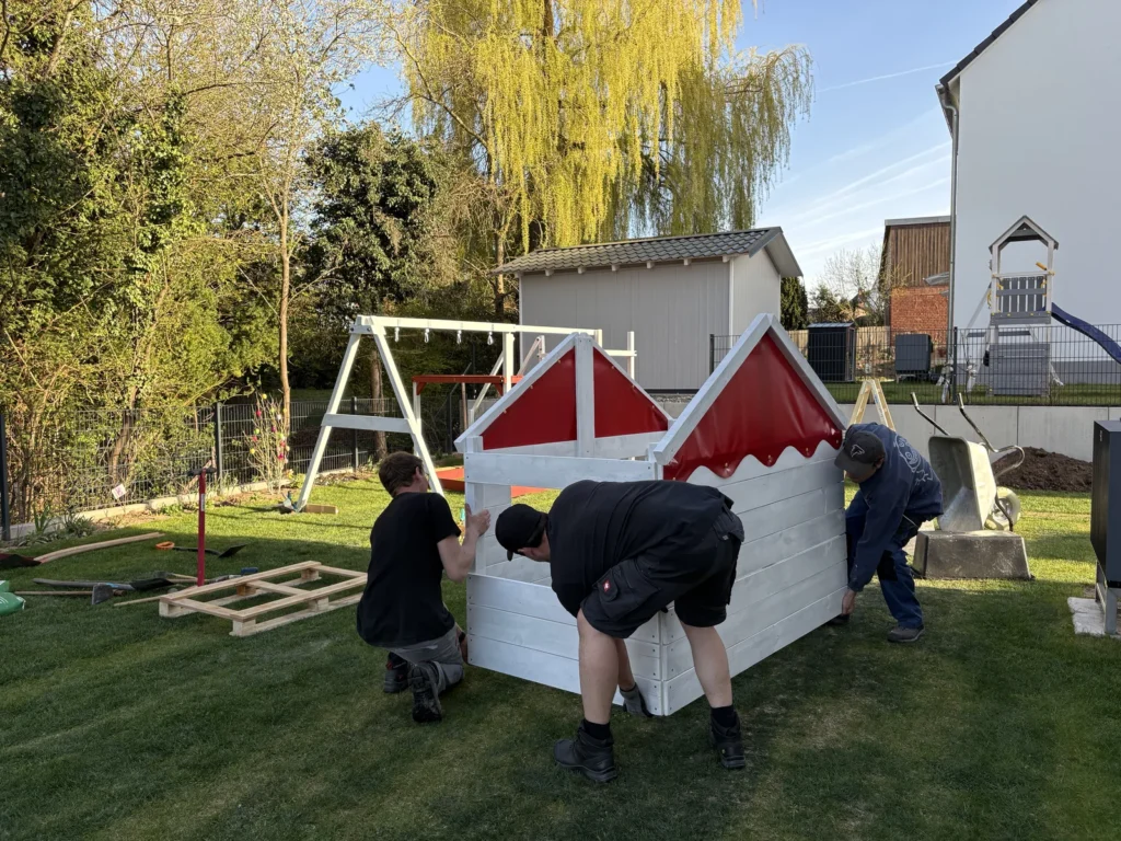 Vier Personen tragen das Spielhaus des Wickey Smart Seaway ohne Dach zum Grundturm