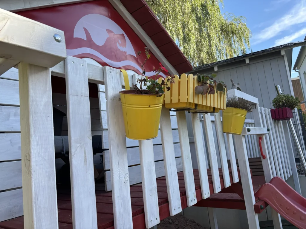 Blumentopf mit Erdbeerpflanze am Geländer vor dem Spielhaus