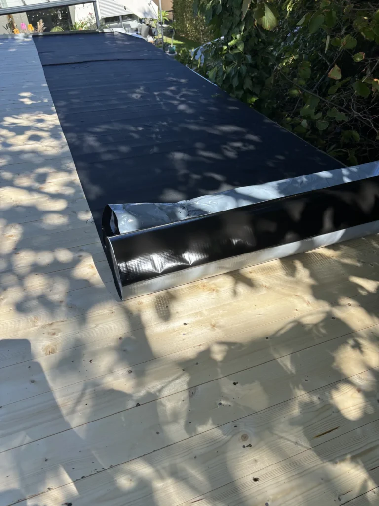 Erste EPDM-Bahn auf dem Gartenhausdach verklebt mit sichtbaren Falten