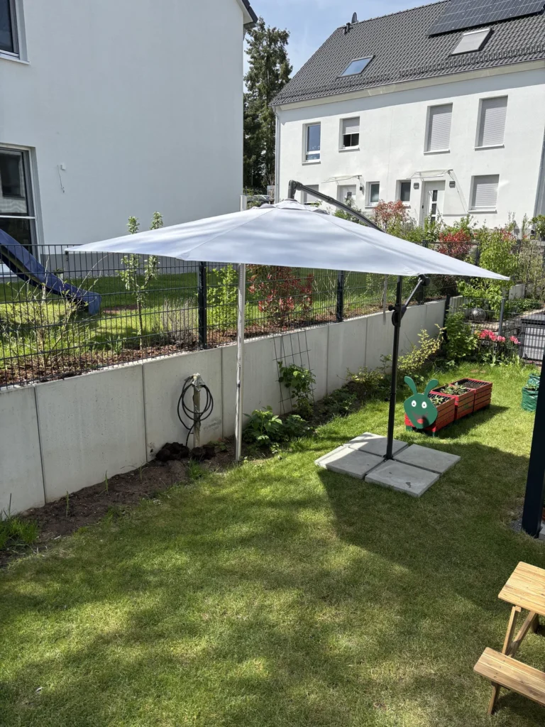 Geöffneter Sonnenschirm mit vier Betonplatten auf der Rasenfläche