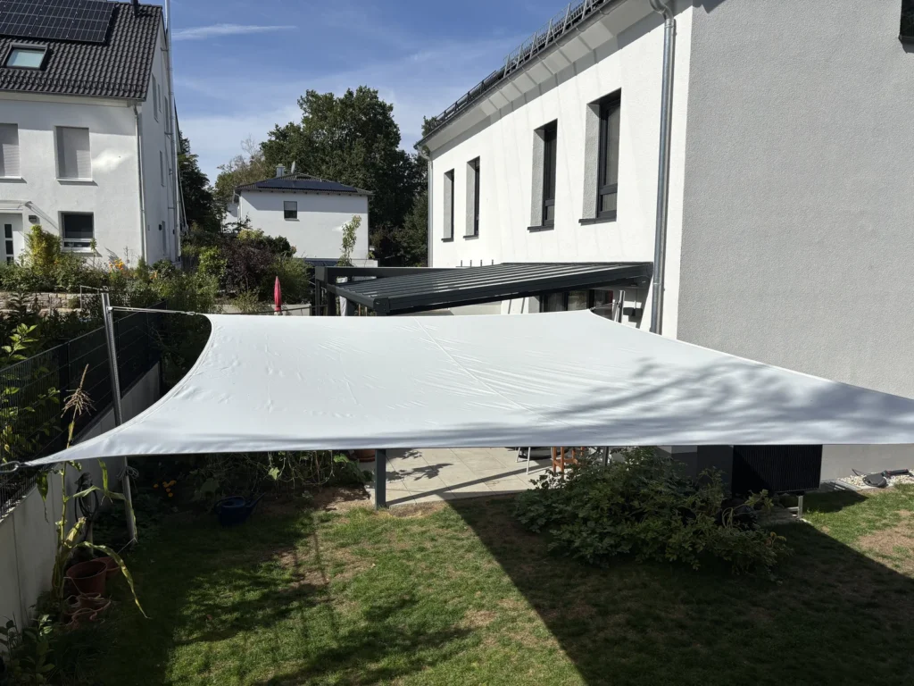 Beschattete Rasenfläche unter dem Sonnensegel zwischen Spielturm und Terrasse