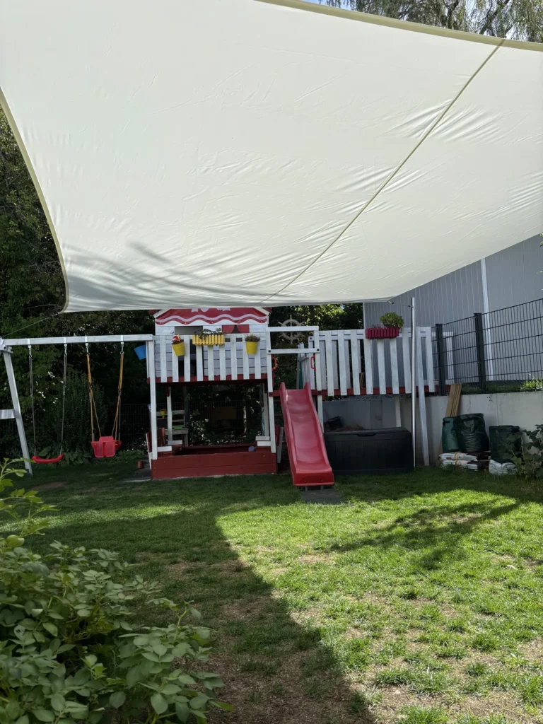 Cremeweißes Sonnensegel von unten mit Spielturm und Mast im Hintergrund