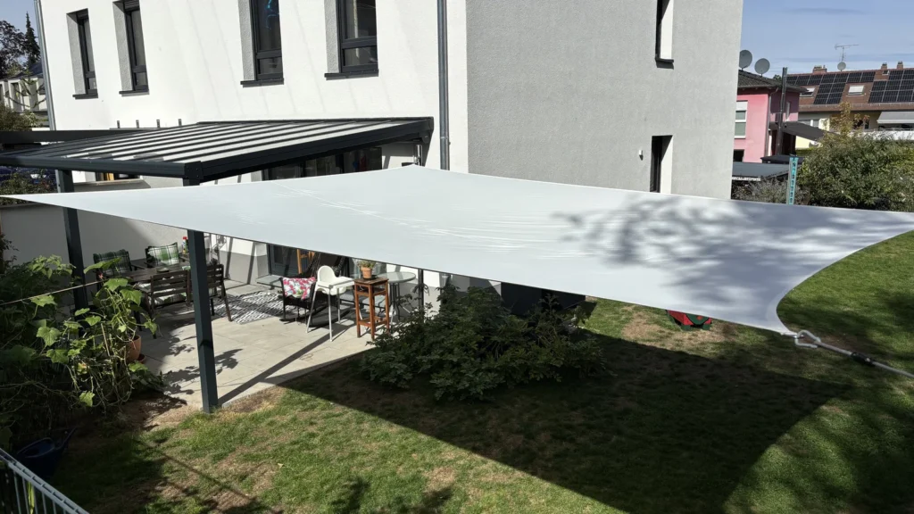Sonnensegel im Garten zwischen Spielturm und Terrasse mit beschatteter Rasenfläche